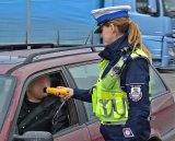 Policjanta w umundurowaniu służbowym, w białej czapce, sprawdza stan trzeźwości urządzeniem ALCOBLOW, kierującego samochodem osobowym koloru bordowego