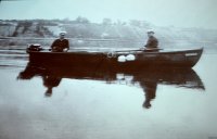 Stare zdjęcie przedstawiające dwóch mężczyzn w mundurach, siedzących w łódce pływającej na wodzie