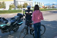 Policjant w umundurowaniu pełniący służbę motocyklem kontroluje cyklistkę.