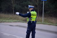 Policjant w umundurowaniu służbowym i kamizelce odblaskowej kieruje ruchem