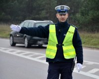Policjant w umundurowaniu służbowym i kamizelce odblaskowej kieruje ruchem