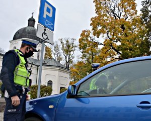 Policjant WRD w umundurowaniu służbowym kontroluje prawidłowość zaparkowania pojazdu na miejscu parkingowym dla osób niepełnosprawnych