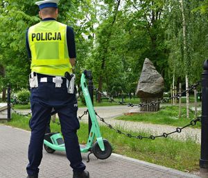 Policjant stoi przy hulajnodze w parku