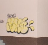 Na beżowej ścianie żółty napis graffiti