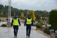 dwóch policjantów w umundurowaniu służbowym, w kamizelkach odblaskowych, na cmentarzu