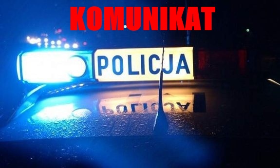 Radiowóz policyjny nocą, nad nim napis czerwonymi literami: KOMUNIKAT.