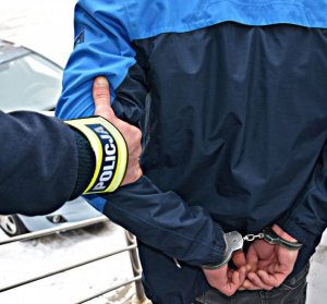 ręka z opaską Policja trzyma zakutego w kajdanki