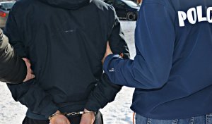 Zatrzymany mężczyzna z kajdankami na rękach doprowadzany przez policjantów