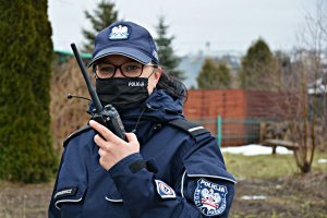 Policjantka w umundurowaniu służbowym rozmawia przez stację na terenie działek