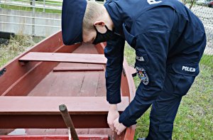 Policjant w umundurowaniu ćwiczebnych pochylony nad łodzią drewnianą