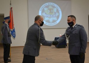 Dwóch policjantów podczas uścisku ręki w tle sztandar