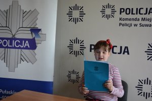 Dziewczynka trzyma teczkę w tle tapeta z napisem POLICJA