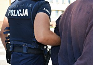 Policjanci w mundurach doprowadzają zatrzymanego