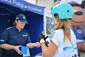 Policjantka w namiocie z napisem Komenda Miejska Policji w Suwałkach, obok zawodniczki, rozmawiają o bezpieczeństwie