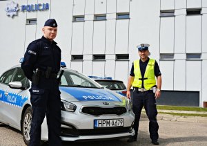 Dwóch policjantów stoi przy radiowozie, w tle budynek KMP Suwałki