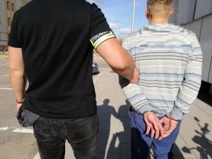 Policjant prowadzi zatrzymanego skutego w kajdanki