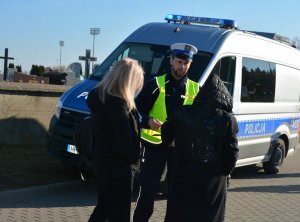 Policjant rozmawia z pieszymi w tle radiowóz