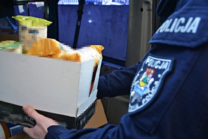 Ręka policjanta z naszywką KMP w Suwałkach, podająca paczkę do samochodu