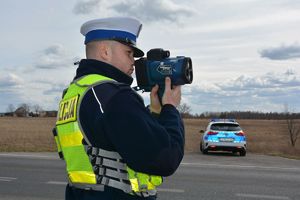 Policjant z radarem w tle radiowóz