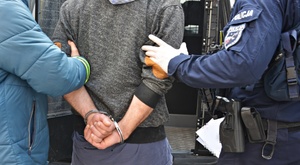 Policjanci doprowadzają zatrzymanego, który ma ręce z tyłu w kajdankach
