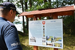 Policjant stoi przy tablicy, opisującej okolicę