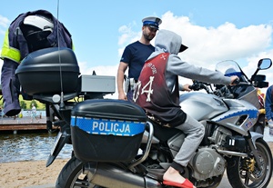 Chłopak na motocyklu policyjnym, w tle policjant i jezioro