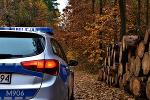 Radiowóz w lesie, w tle przebarwione jesiennie drzewa