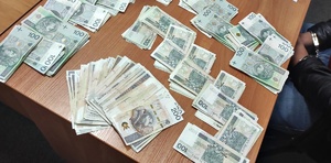Pieniądze, banknoty porozkładane na stole, obok zatrzymany- widać ręce w kajdankach