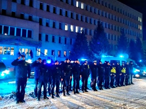Noc, policjanci stoją przed budynkiem, oddają honor