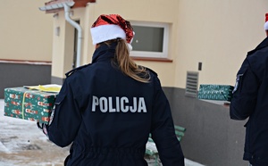 Policjanci w mikołajkowych czapkach na głowach niosą paczki