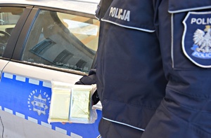 Policjant z kocami termicznymi w ręku na tle radiowozu
