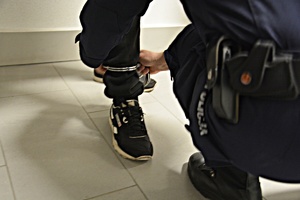 Policjant zakłada kajdanki na nogi poszukiwanemu
