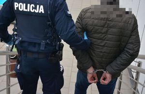 Policjant prowadzi mężczyznę skutego w kajdanki