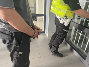 męskie ręce skute w kajdankach obok fragment policjanta