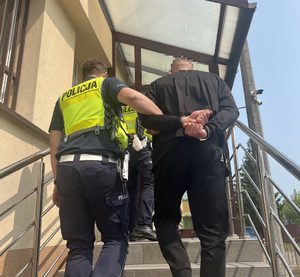 Policjant prowadzi mężczyznę w kajdankach