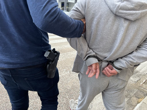 ręce mężczyzny skute w kajdanki obok policjant z bronią