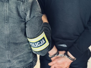 Policjant prowadzi zatrzymanego w kajdankach