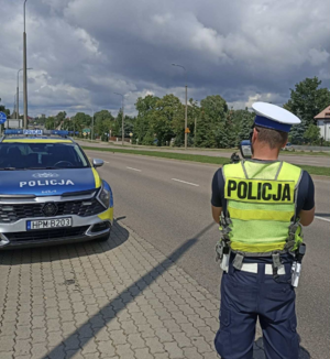 policjant dokonuje pomiaru prędkości w tle droga i samochód służbowy