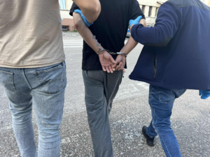 mężczyzna skuty w kajdanki prowadzony przez policjantów