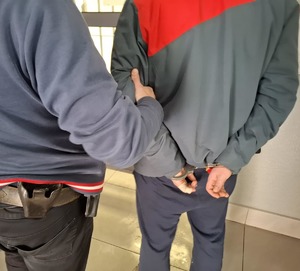 osoba zatrzymana w kajdankach obok niumundurowany policjant