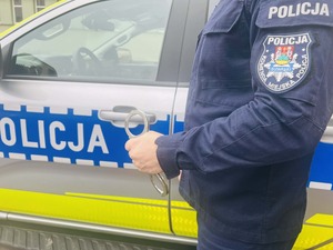 policjant z kajdankami w ręku na tle radiowozu