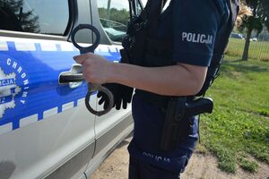 policjanta trzyma kajdanki w tle radiowóz